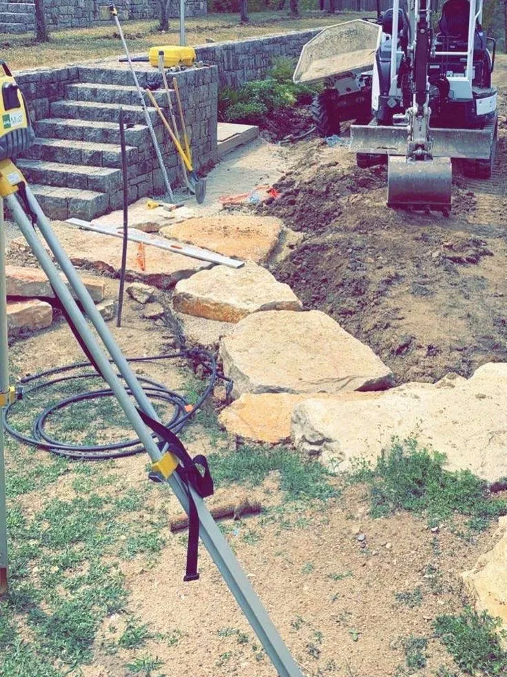Terrain terrassé à la mini-pelle au pied d'un escalier en pierre, grandes dalles calcaires en cours de pose