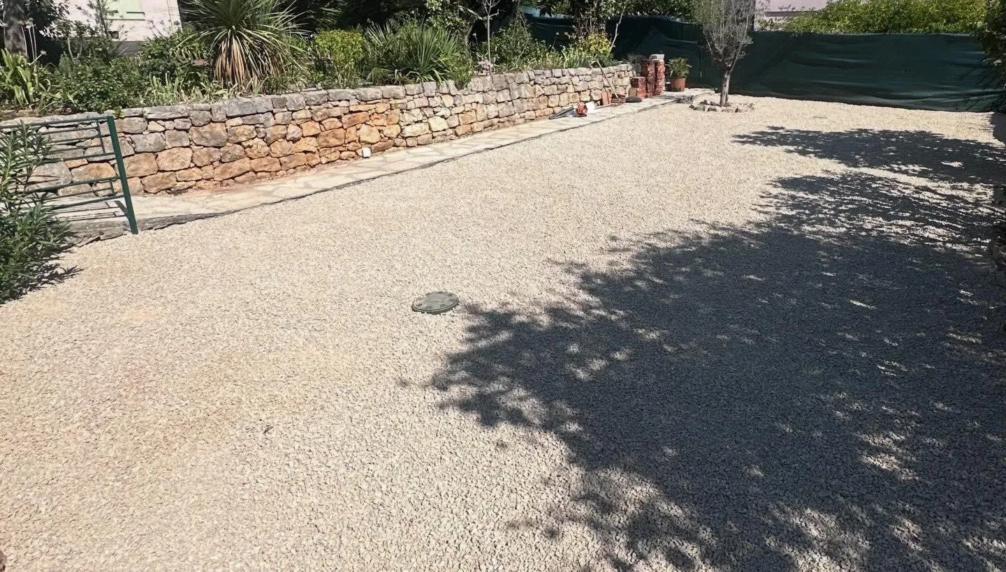 Cour recouverte de gravier clair le long d’un muret en pierre